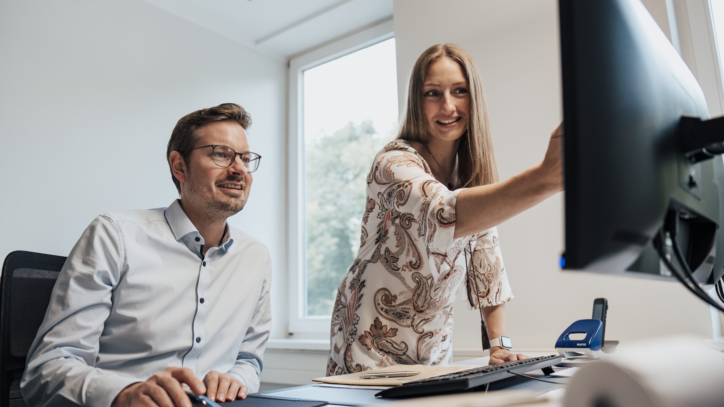 Mann im Hemd und Brille und Frau in Kleid am Schreibtisch im Büro