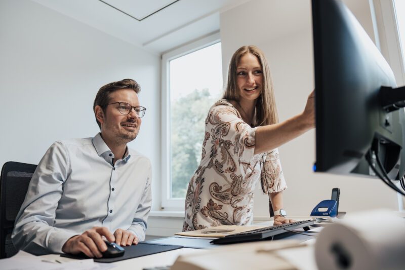 Mann im Hemd und Brille und Frau in Kleid am Schreibtisch im Büro